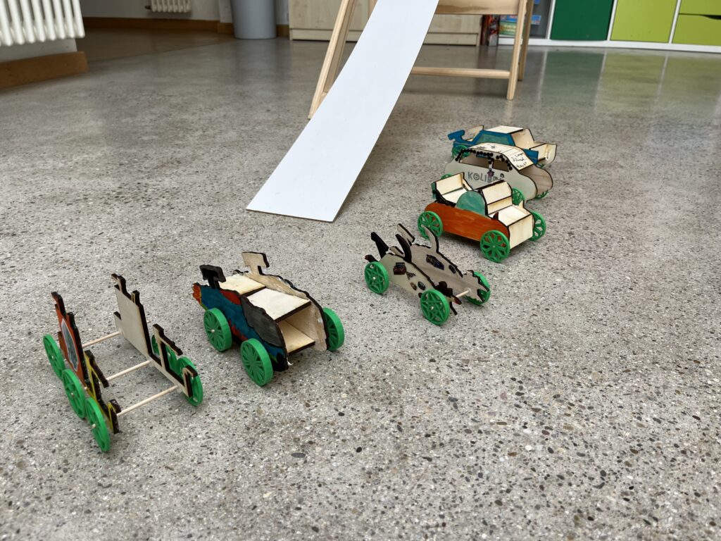 6 selbstgebaute Autos aus Holz stehen neben der Startrampe.