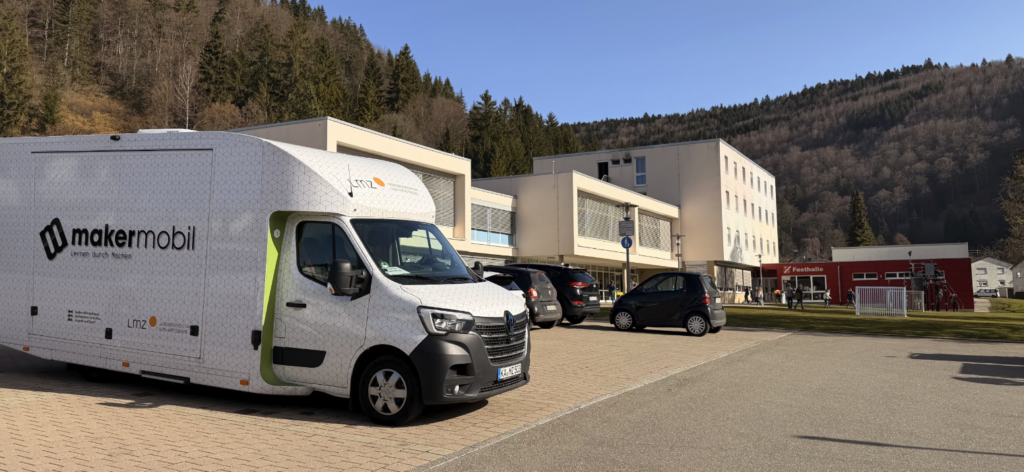 Makermobil vor einer Schule im Kreis Tuttlingen, ein paar mehr Autos und das Schulgebäude im modernen Stil. Weiß und kastenförmig