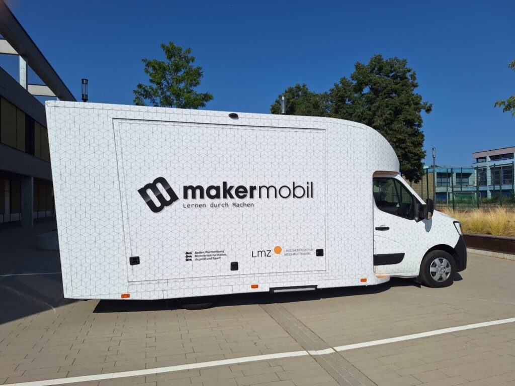 Makermobil auf sonnigem Schulhof, Seitenansicht mit Logo „Lernen durch Machen" und LMZ-Logo.