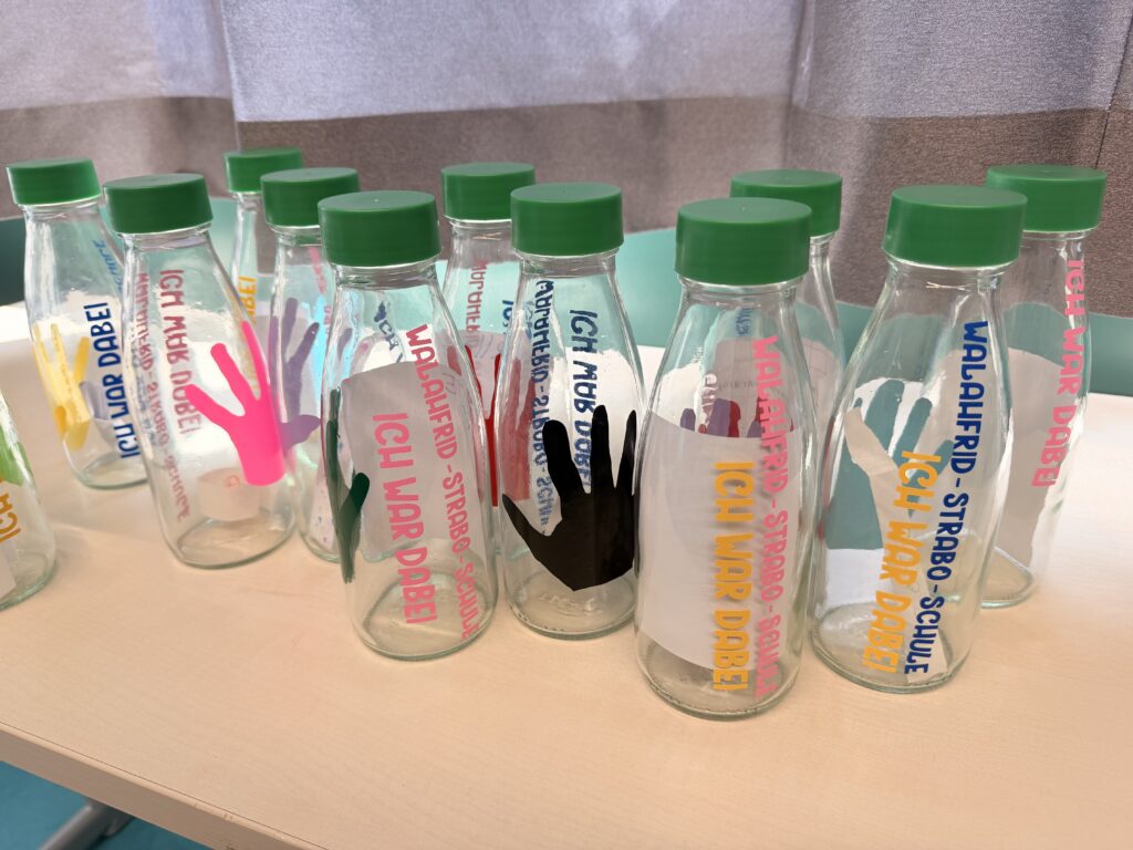 Fertig gestaltete Trinkflaschen mit grünem Deckel, individuellen Handabdrücken in verschiedenen Farben und dem Schriftzug „Ich war dabei – Walahfrid-Strabo-Schule